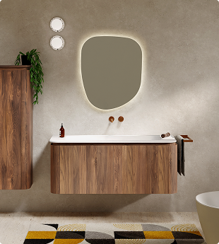 Organisch gevormde spiegel met ledverlichting boven een houten wastafel en kleurrijk vloerkleed.